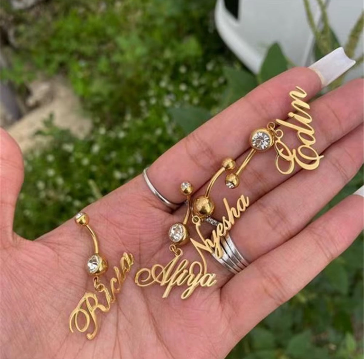 Gold name belly buttons on a hand with a blurred green background