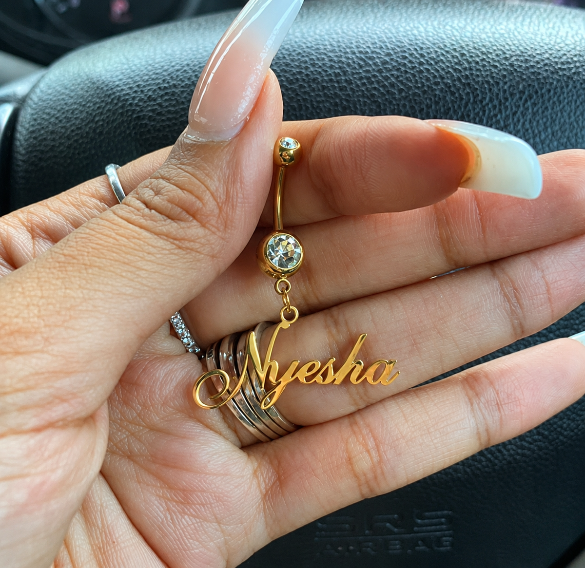 Gold name earring with 'Nyesha' held in a hand against a car interior background