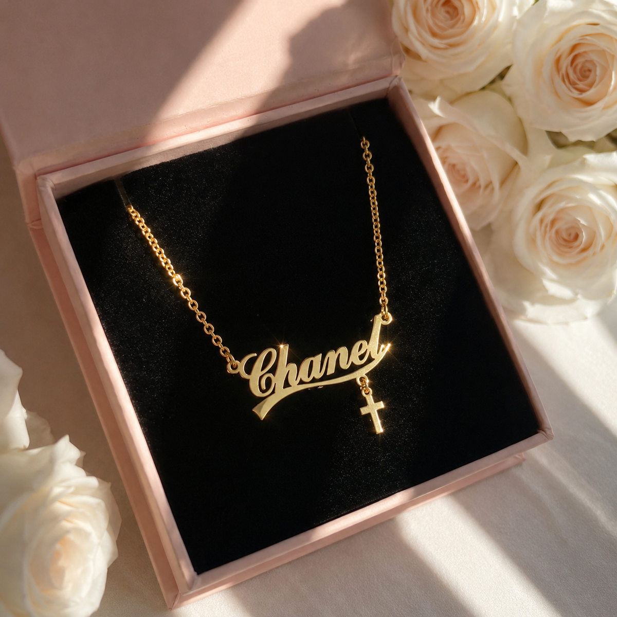 Gold necklace with 'Chanel' on a black cushion in a pink box with white roses.