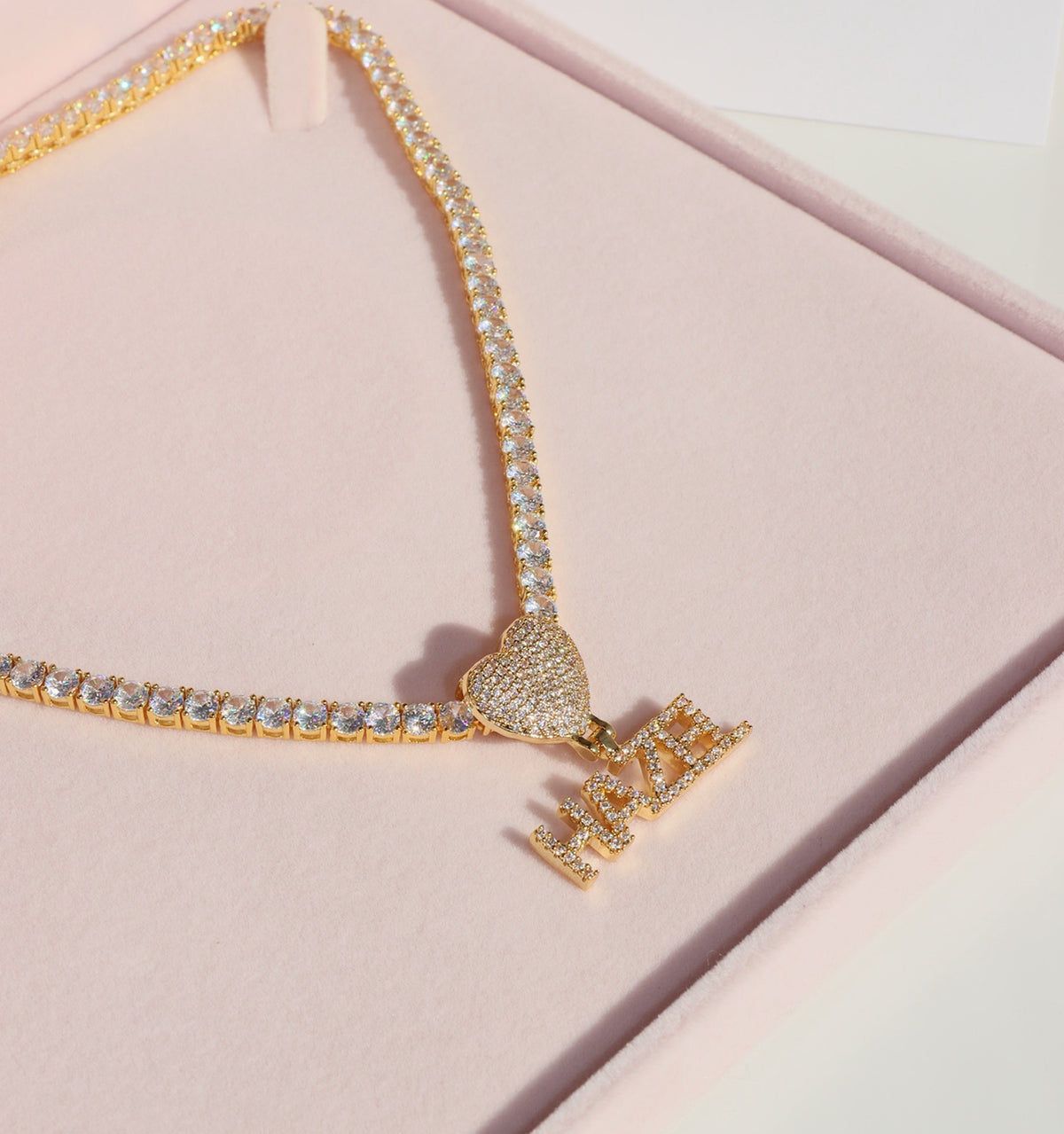 Gold necklace with a crown pendant on a pink background
