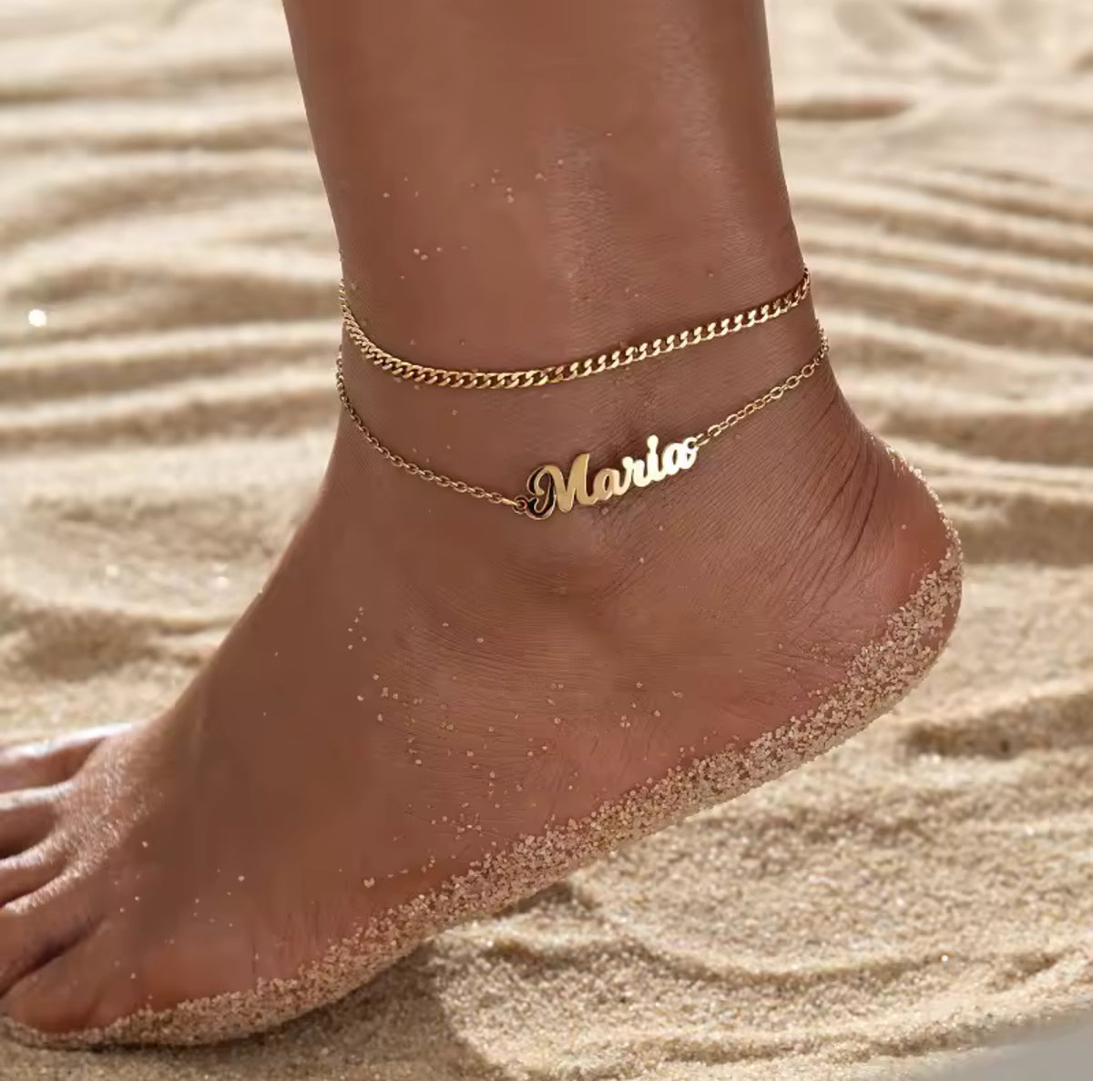 Gold anklet with 'Maria' on a foot in sand