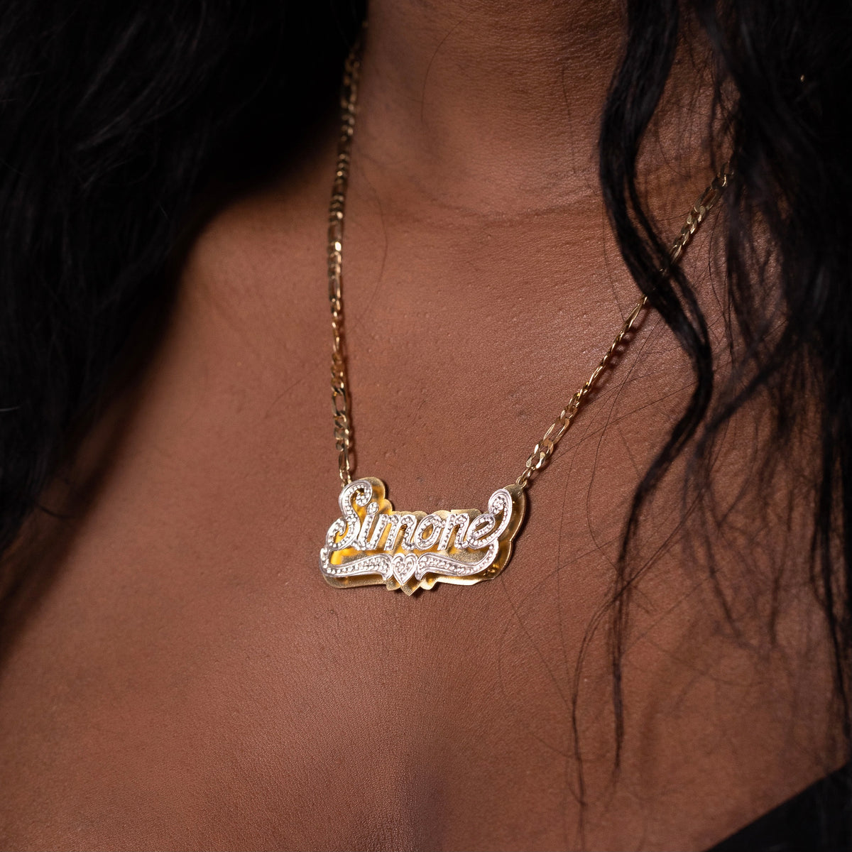 Woman wearing custom name necklace that says Simone. Wearing a black top