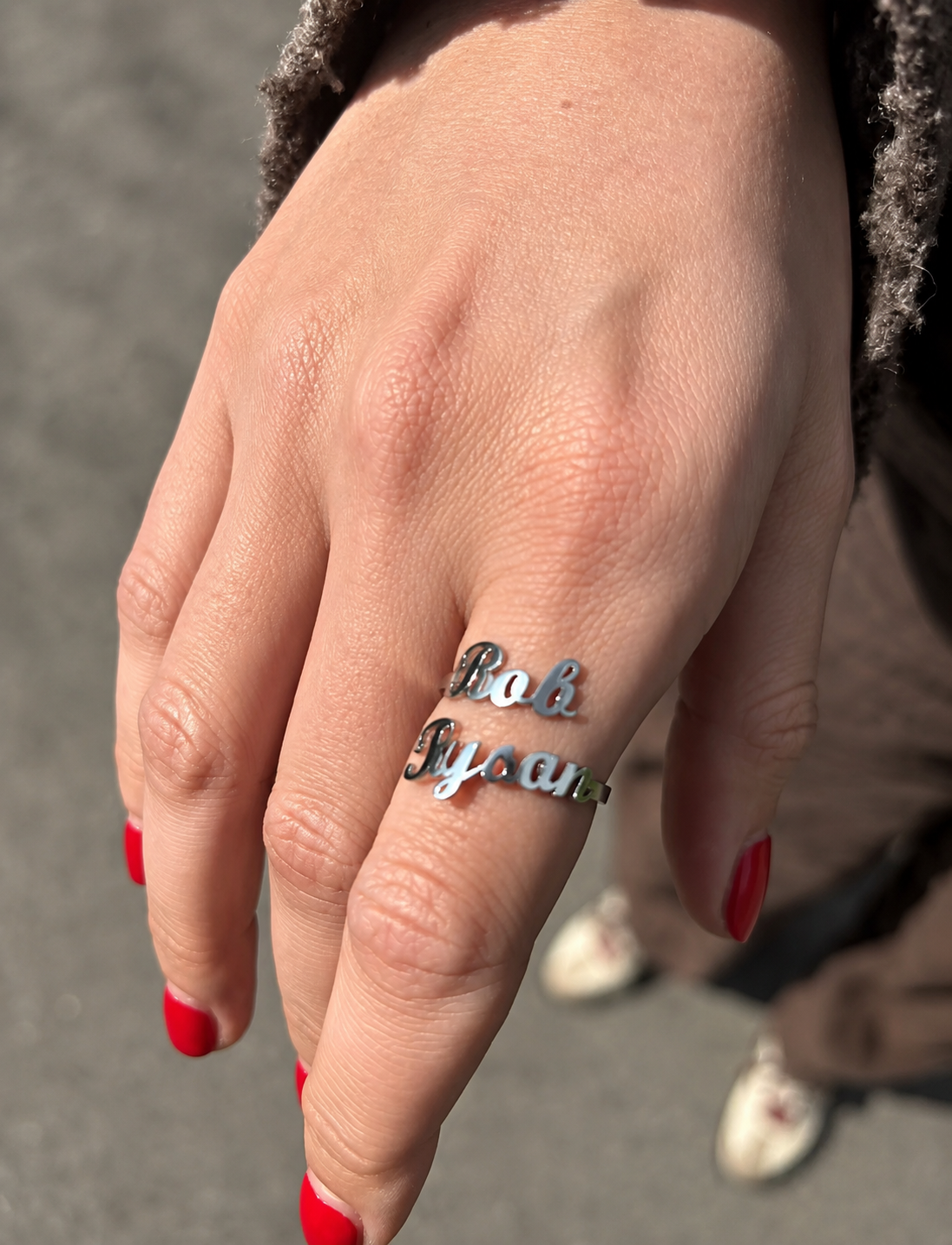 Hand wearing a silver ring with 'Bob Dylan' engraving on a neutral background