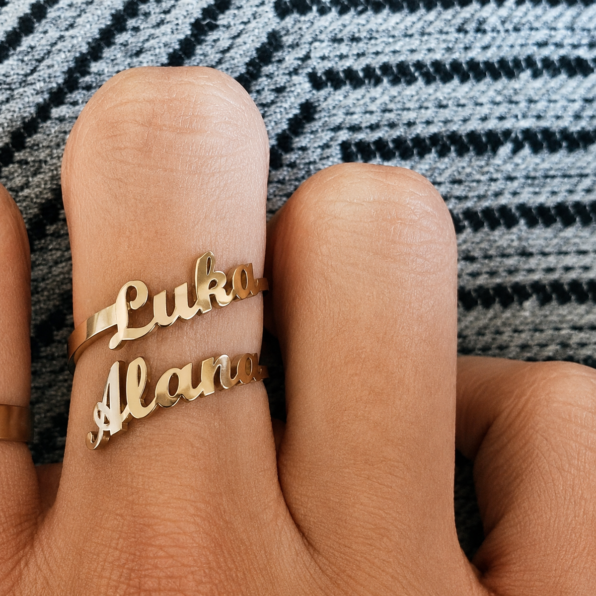 Gold name ring on a finger with a patterned fabric background