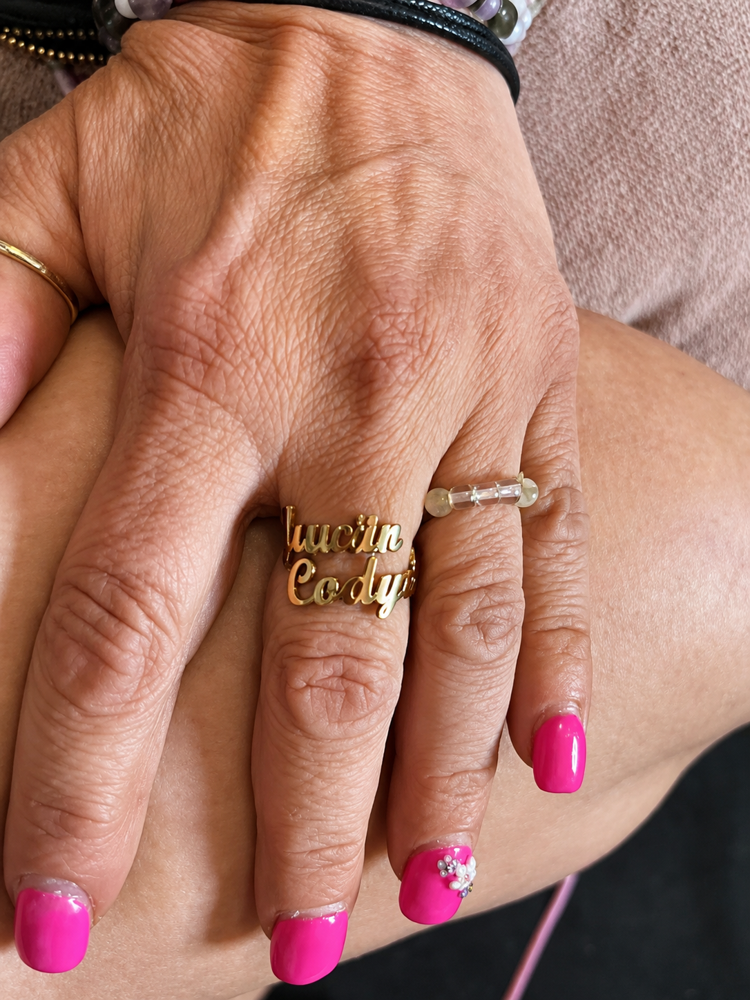Close-up of a hand with pink nail polish wearing two gold rings.
