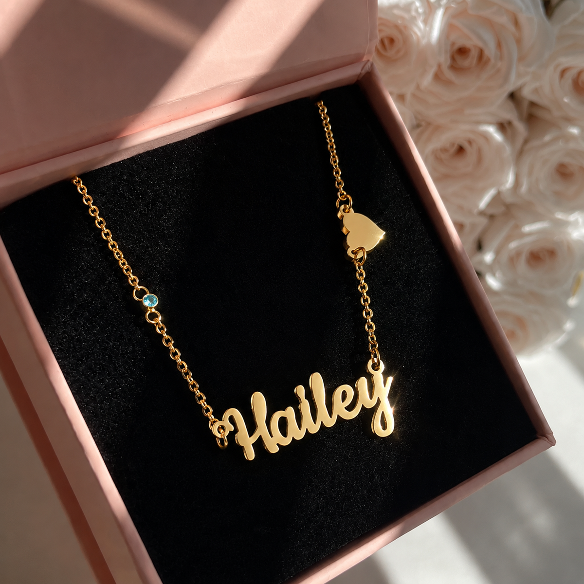 Gold necklace with 'Hailey' pendant in a pink box with flowers in the background