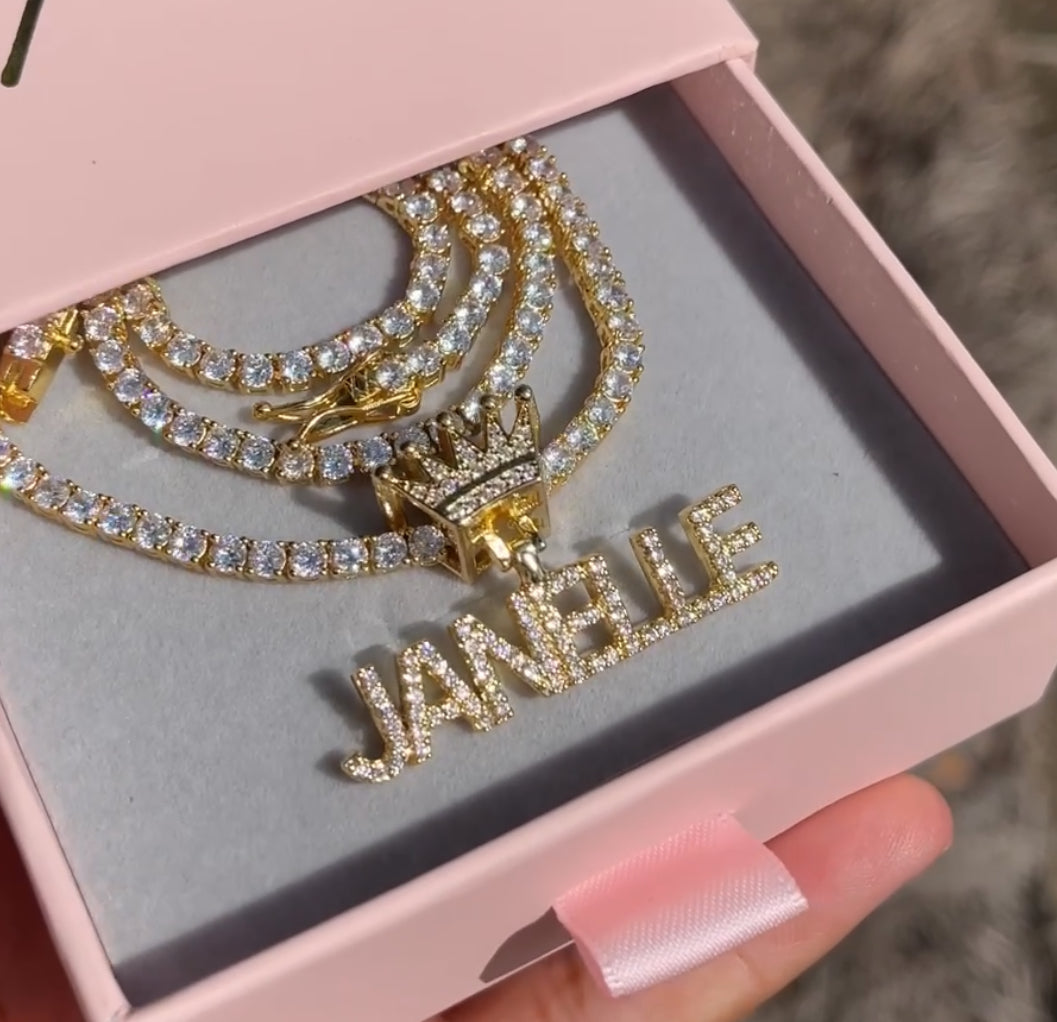 Gold jewelry set with 'JANEBIE' pendant in a pink box.