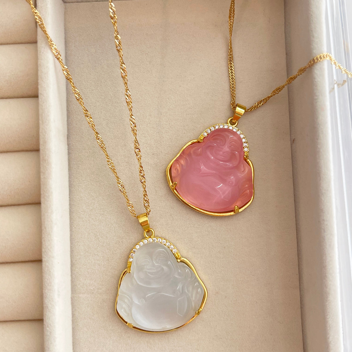 2 Buddha pendants on a beige background. One white and the other pink