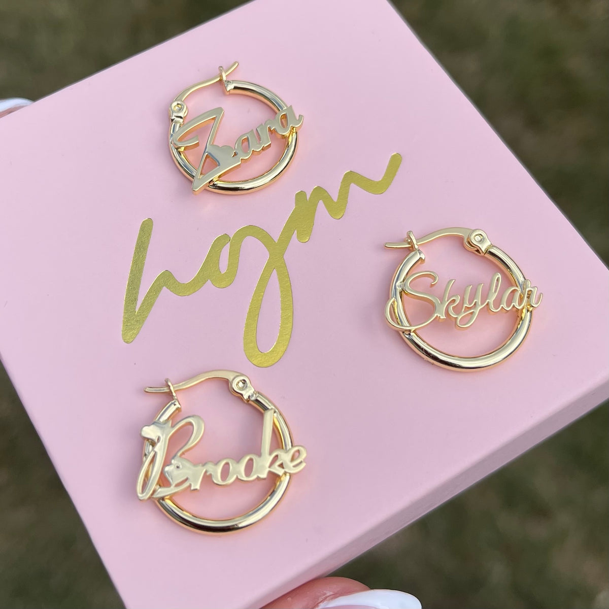 Gold hoop earrings with names on a pink card