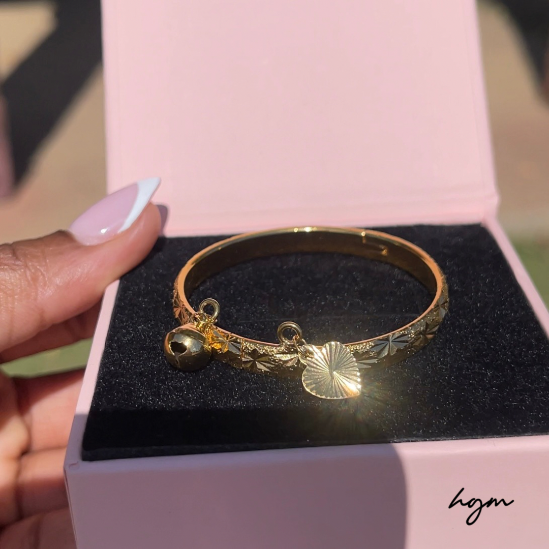 Gold bracelet with charms on a black cushion inside a pink box, held by a hand.