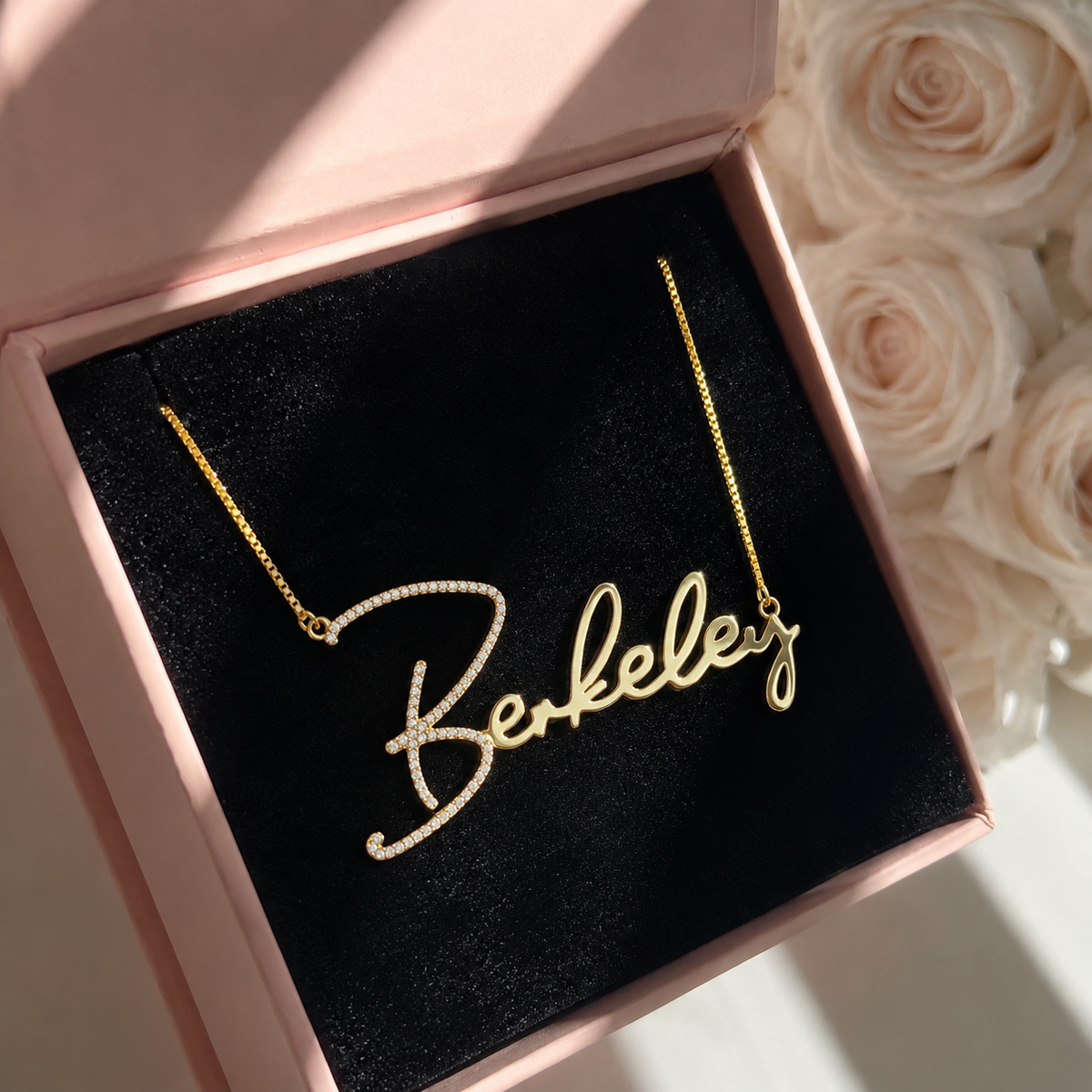 Gold necklace with 'Berkeley' inscription in a pink box with flowers in the background