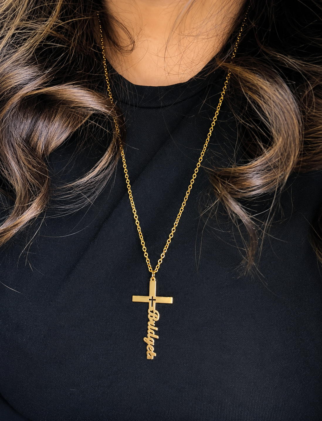 Gold necklace with a cross pendant worn by a person against a black background