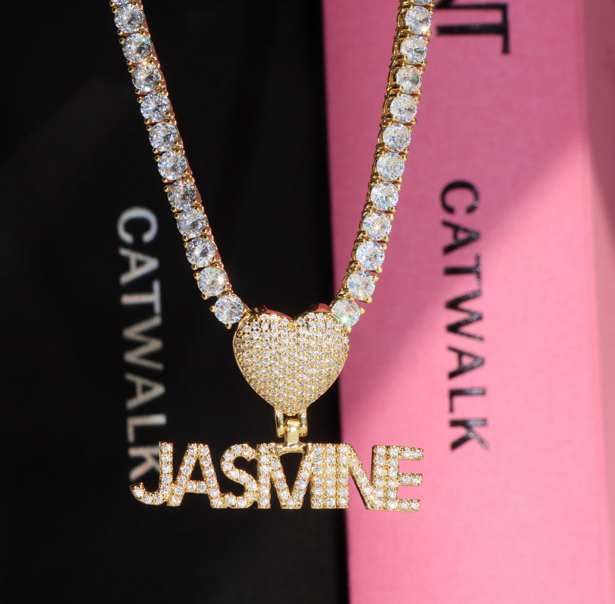 Gold necklace with heart pendant and 'JASMINE' letters on a black and pink background