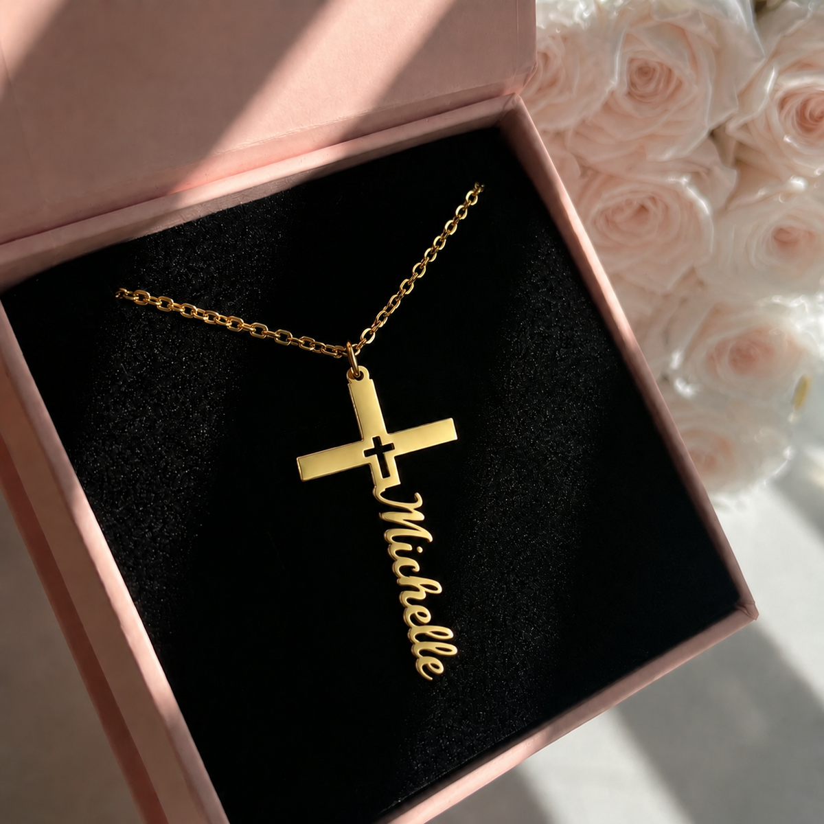 Gold necklace with a cross and 'Michelle' engraving in a pink box with flowers in the background
