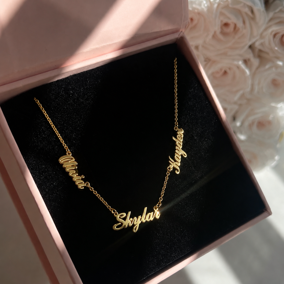 Gold name necklace in a pink box with floral background