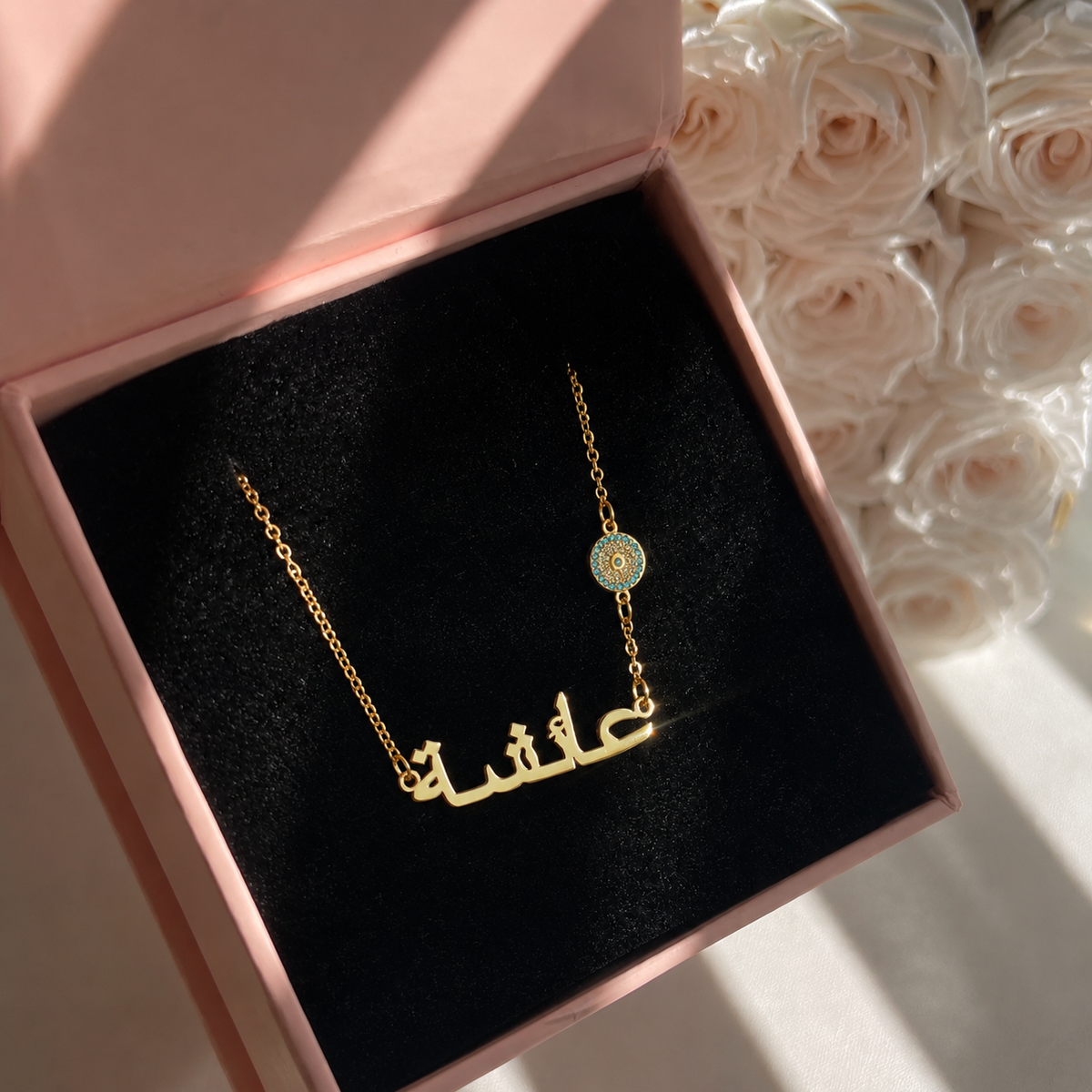 Gold necklace with Arabic script in a pink box with black interior, roses in the background