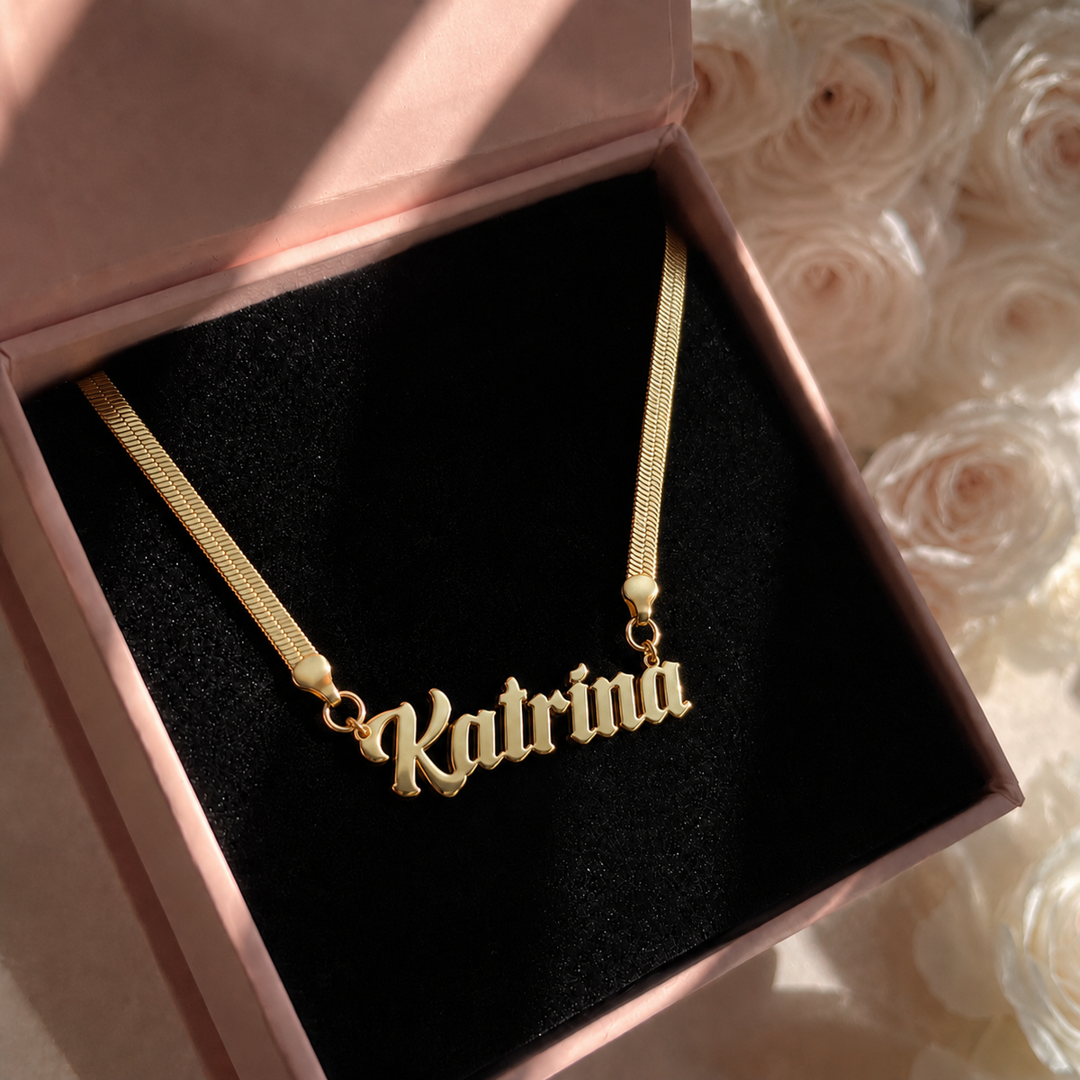 Gold necklace with 'Katrina' pendant in a pink box with roses in the background