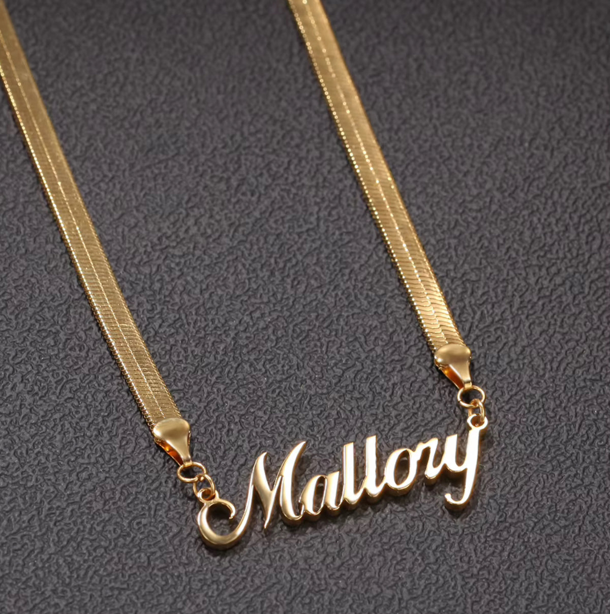 Gold necklace with 'Mallory' pendant on a dark textured background