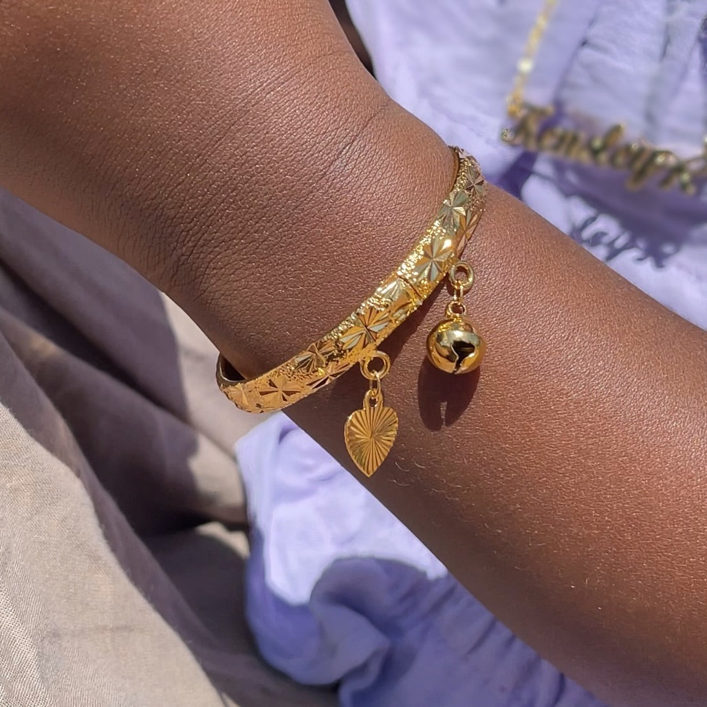 Gold bracelet with charms on a wrist against a neutral background
