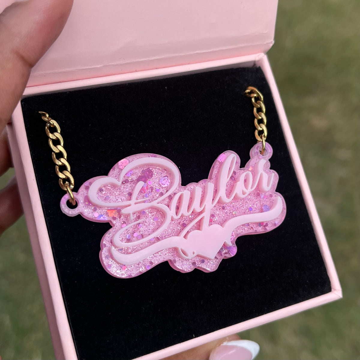 Pink glittery necklace with 'Baylee' on a black box